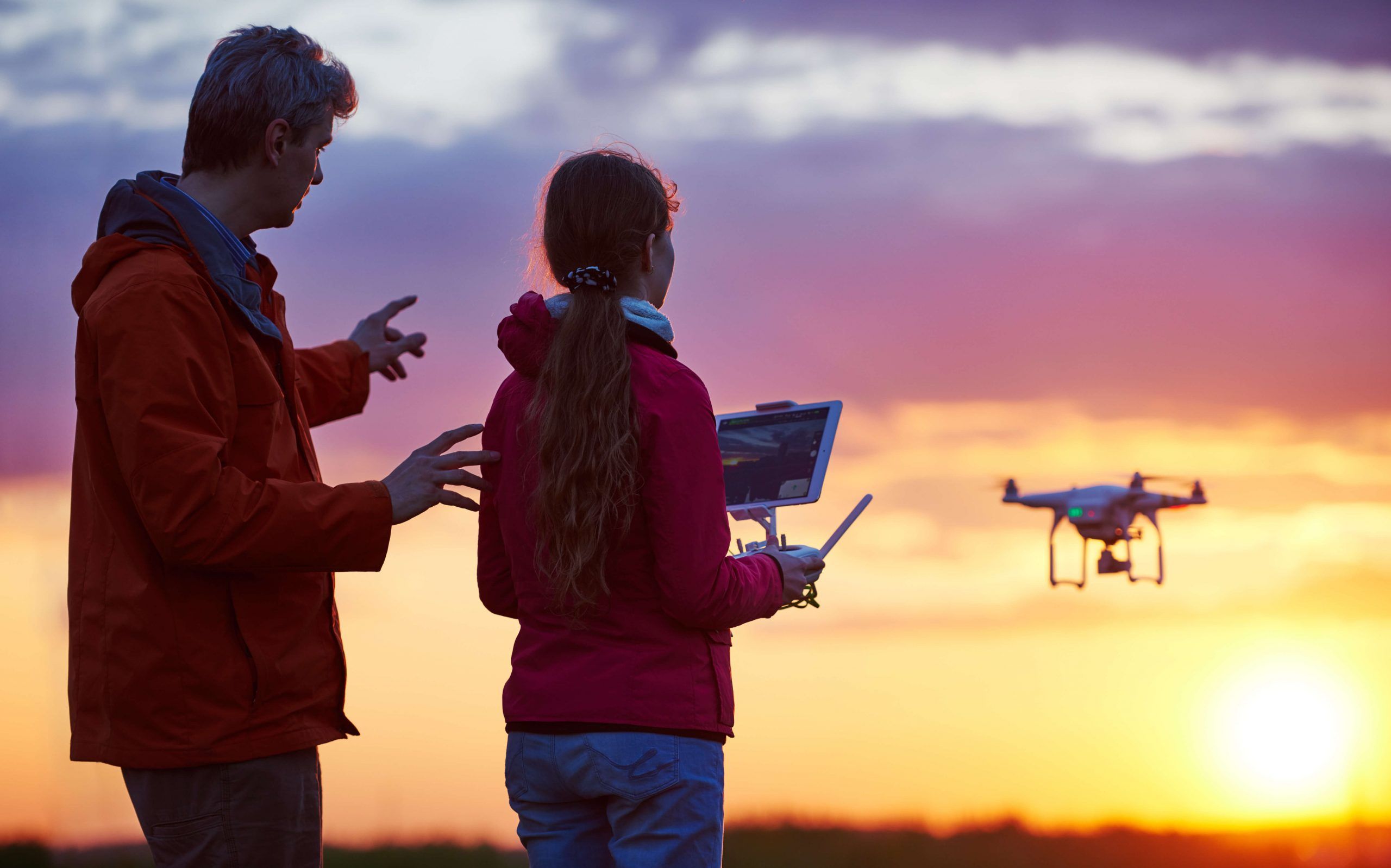 Two drone operators using photogrammetry software on tablet in front of sunset