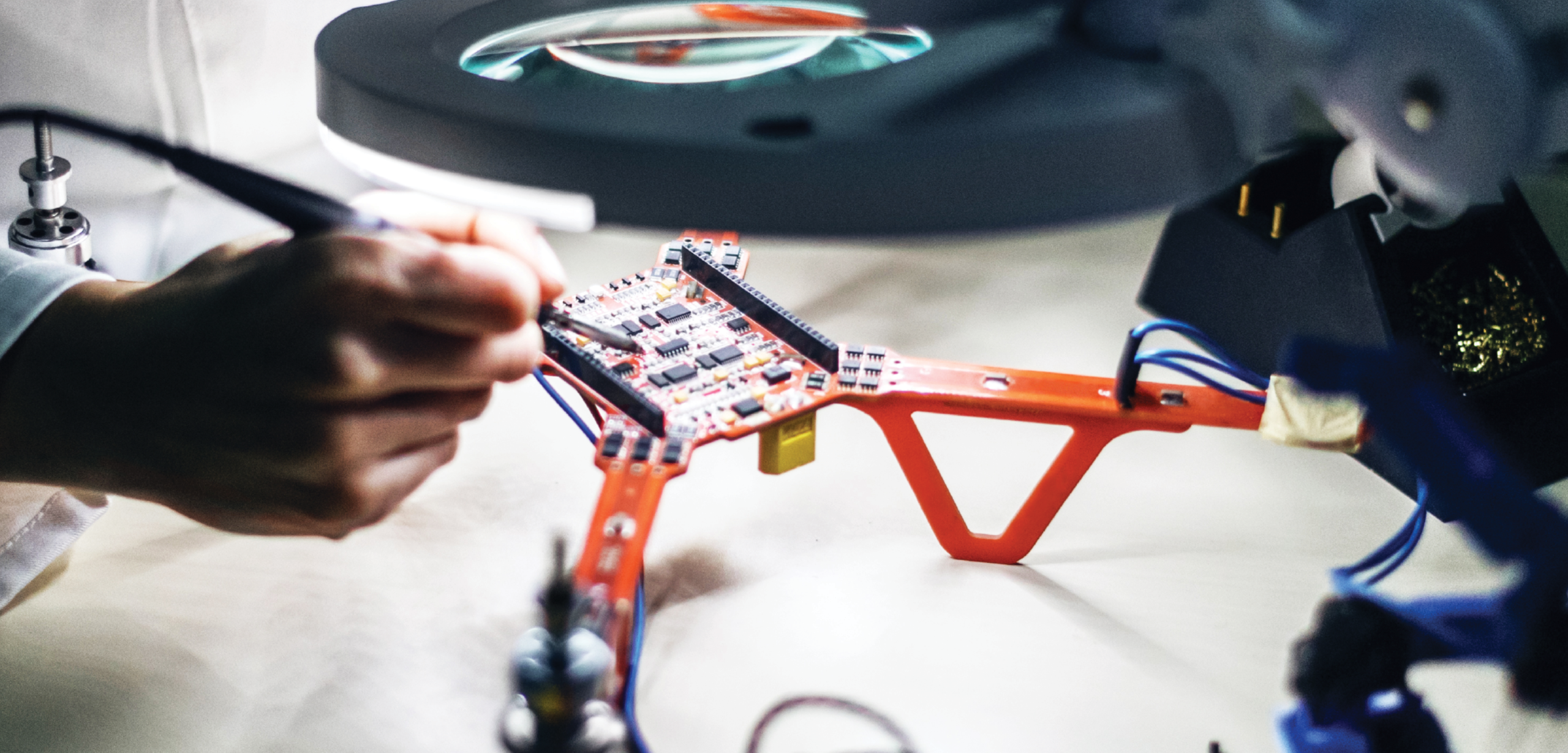 A drone airframe sits open on a table while a technician solders its motherboard.